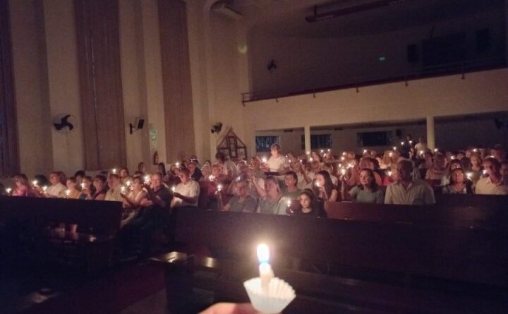 Foto escura, com velas acesas em um culto
