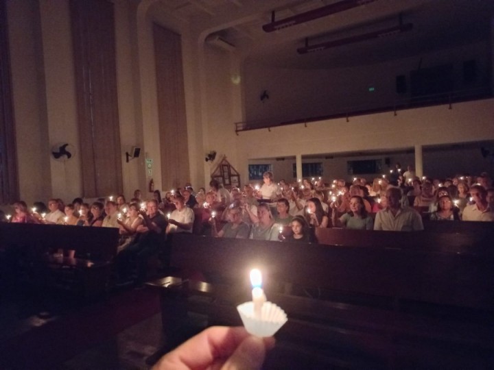 Foto escura, com velas acesas em um culto